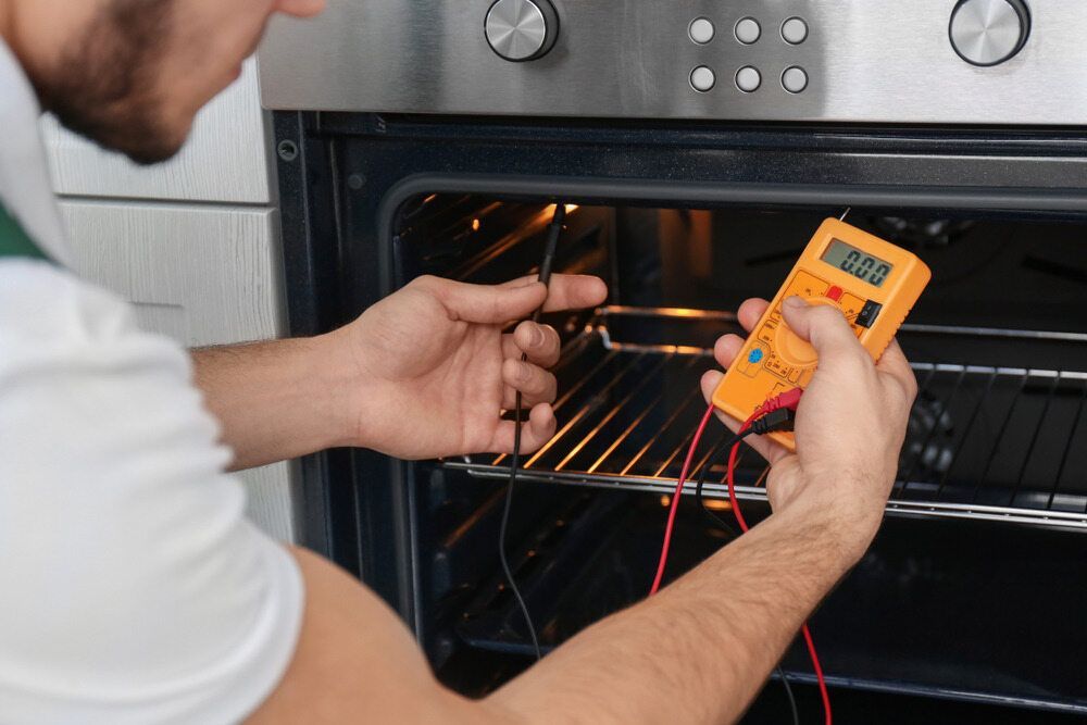 A Man is Fixing an Oven With a Multimeter — Big Bang Electrical And Air In Trinity Park, QLD