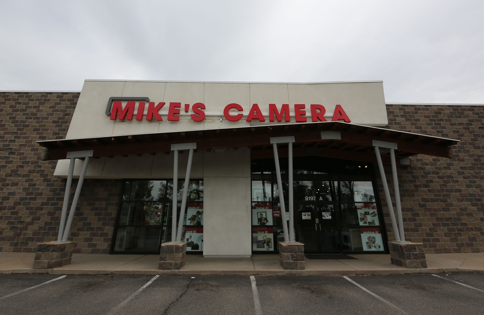 Mike's Camera storefront with red sign, brick accents, and angled roof supported by silver beams.