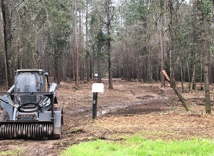 Small bulldozer parked at the edge of a wooded clearing with a dirt path and signpost nearby.