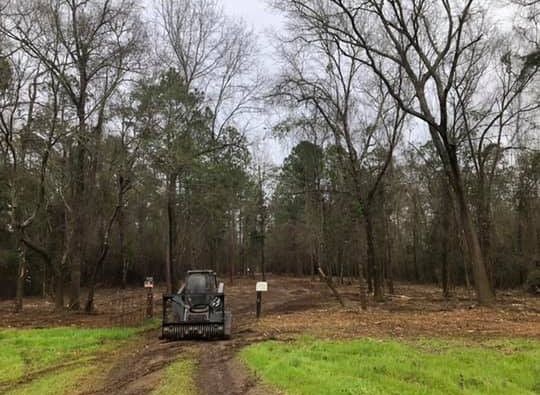 A muddy trail leads to a black off-road vehicle in a leafless forest