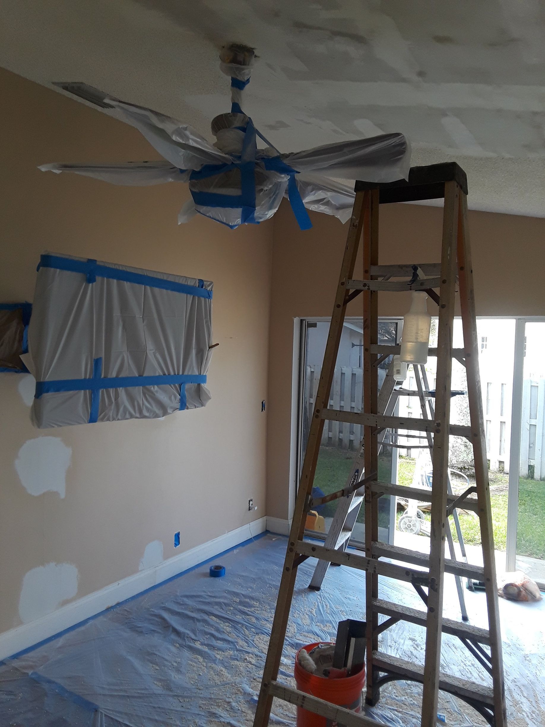 A room is being painted and a ceiling fan is hanging from the ceiling.