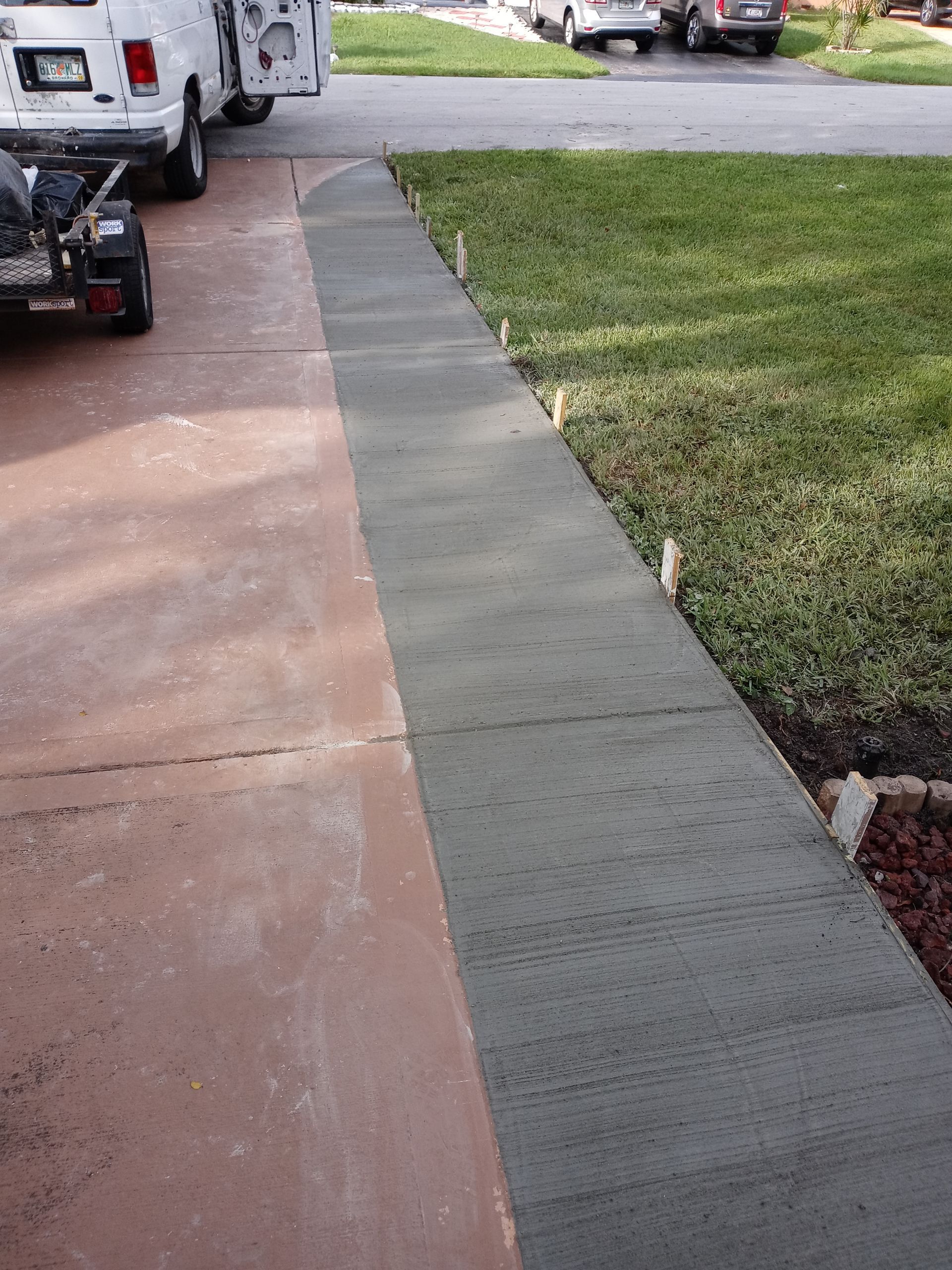 A white van is parked in a driveway next to a sidewalk.