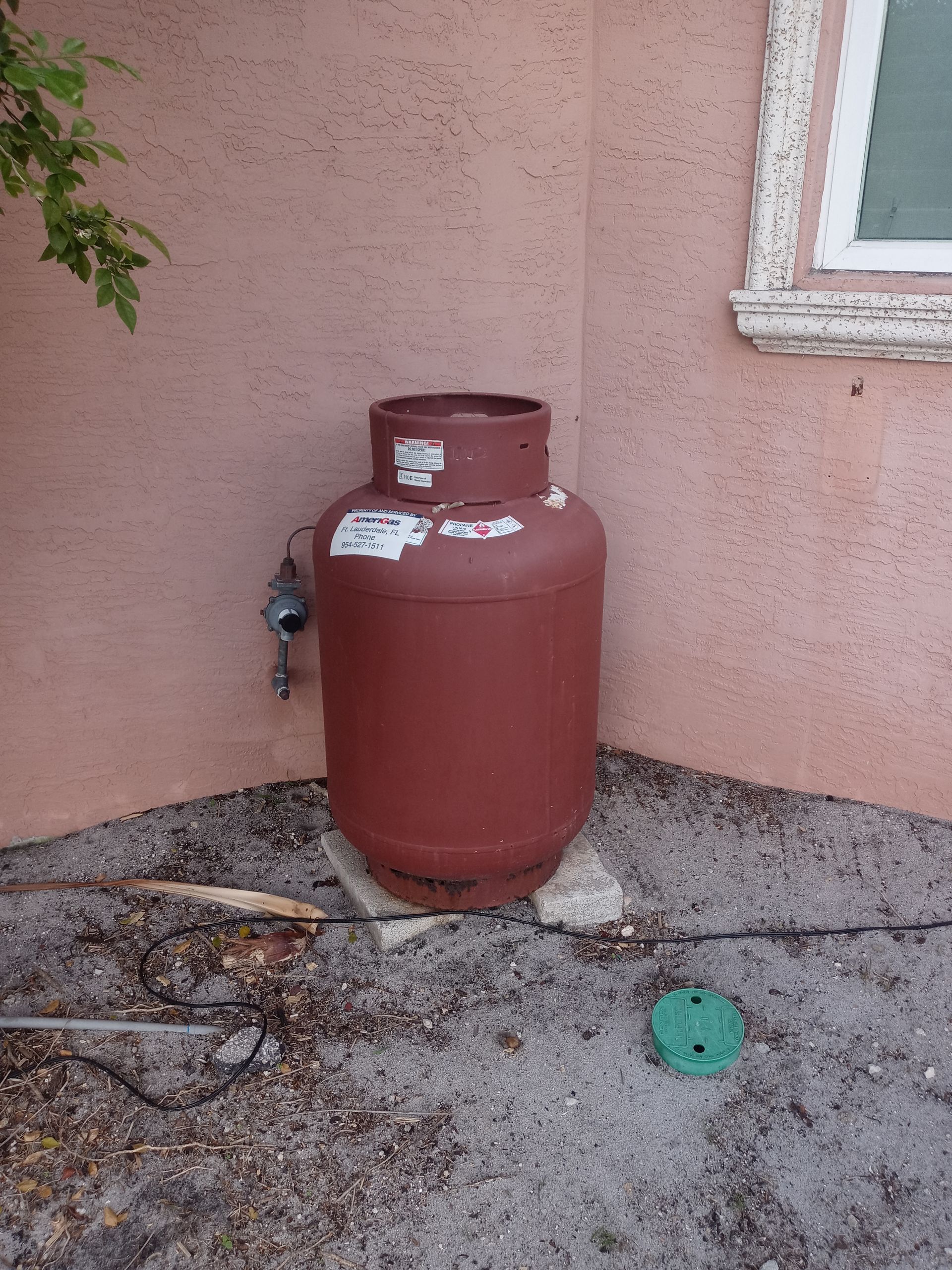 A red propane tank is sitting in the corner of a house.