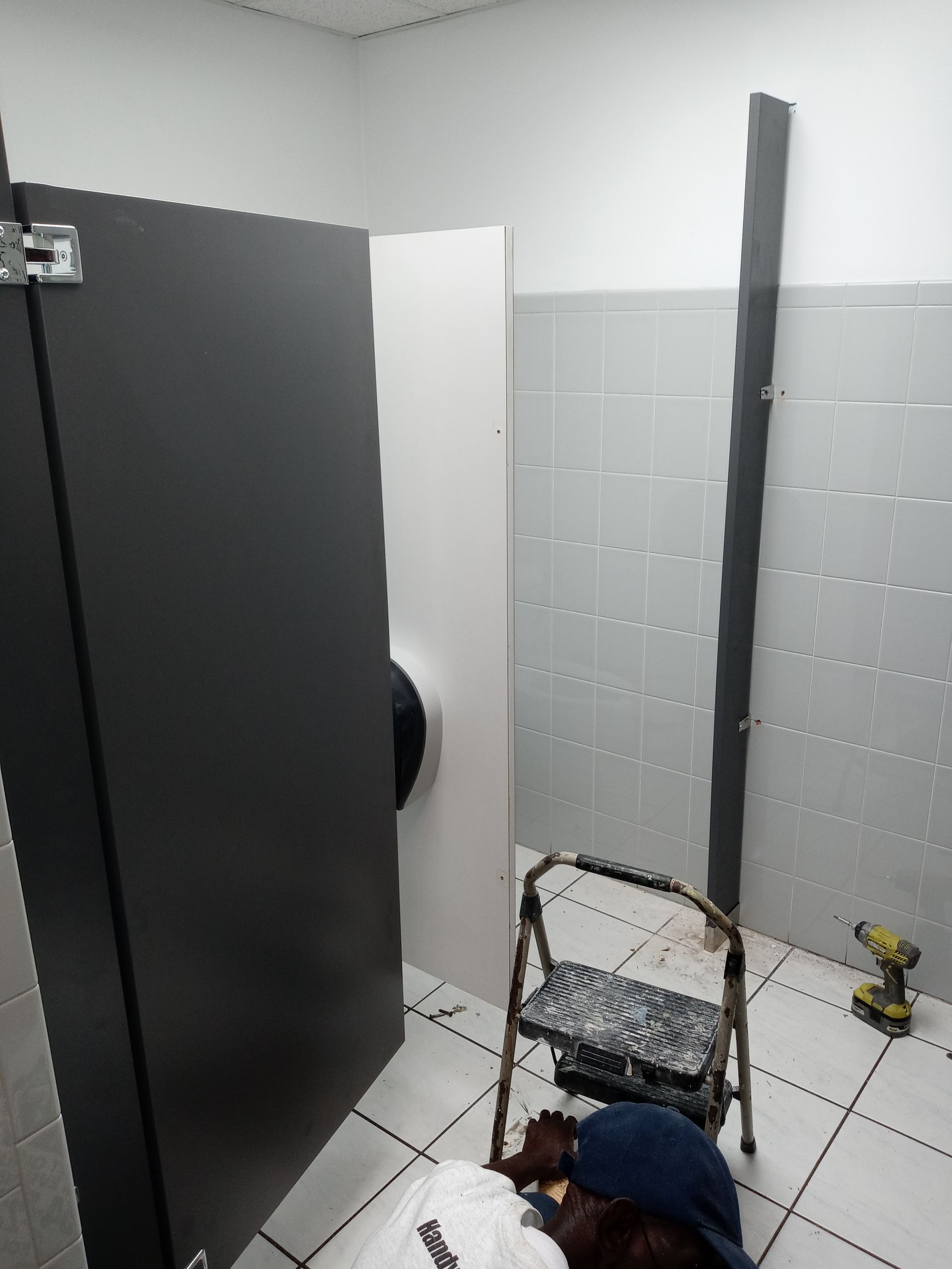 A person is standing in a public restroom next to a ladder.