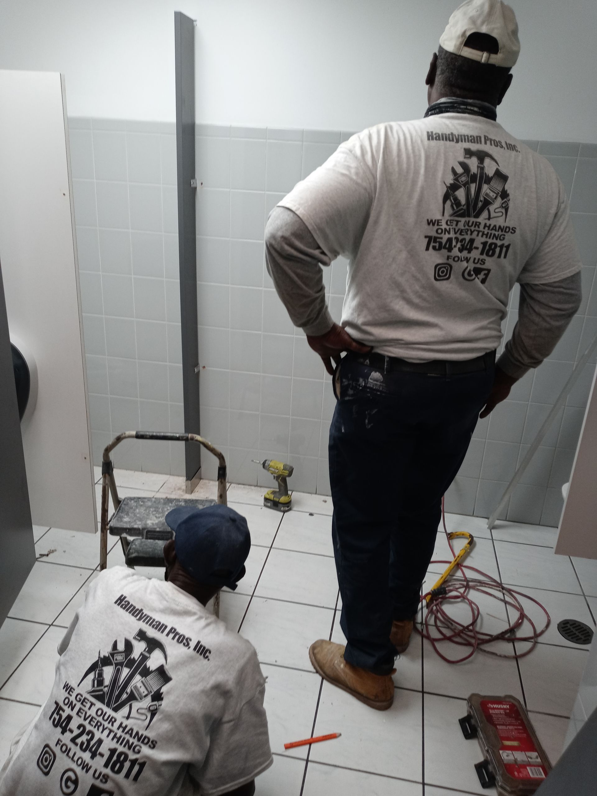 Two men are working in a bathroom and one has the number 734-8877 on his back