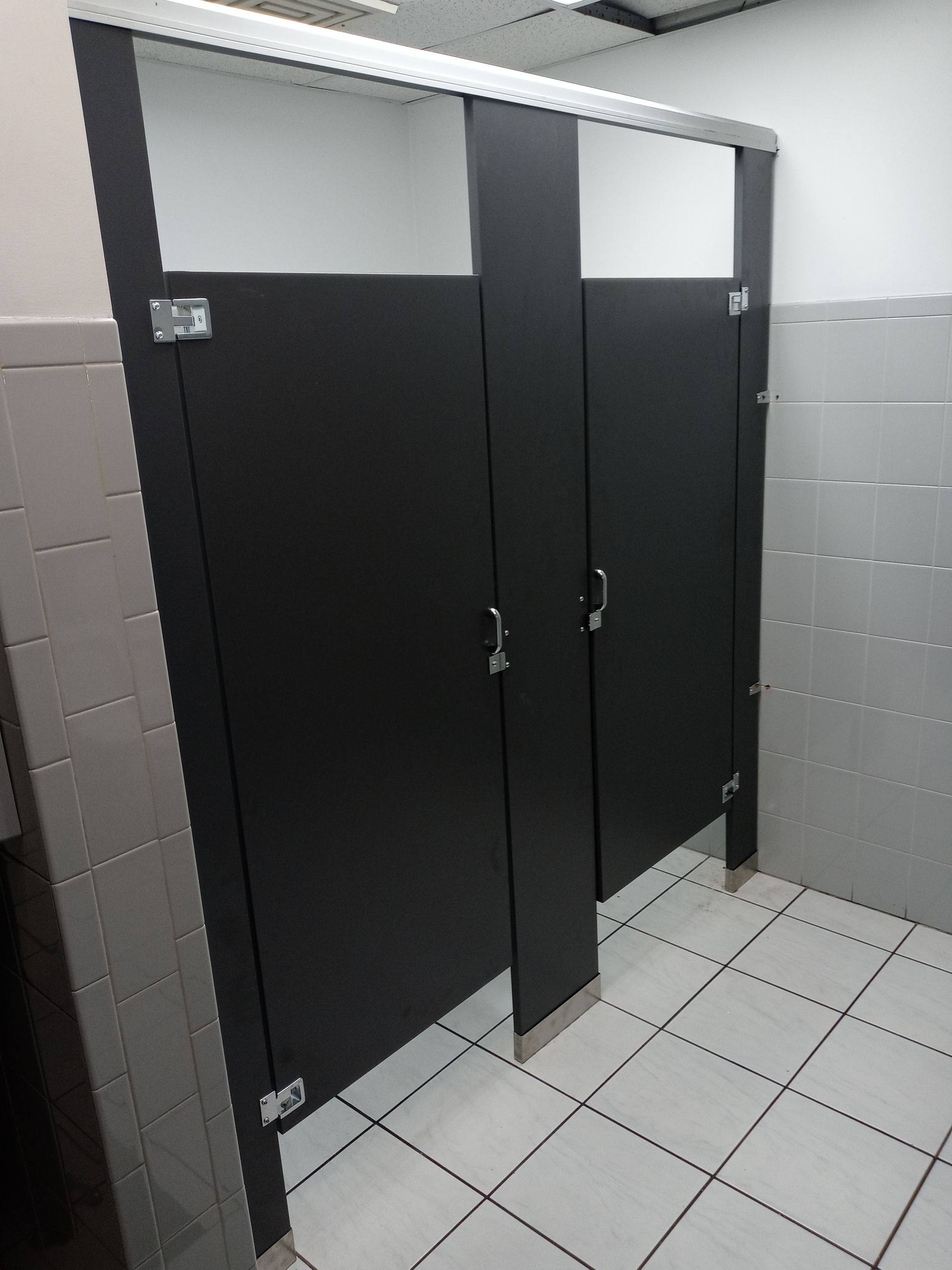 A public restroom with black stalls and white tile floors