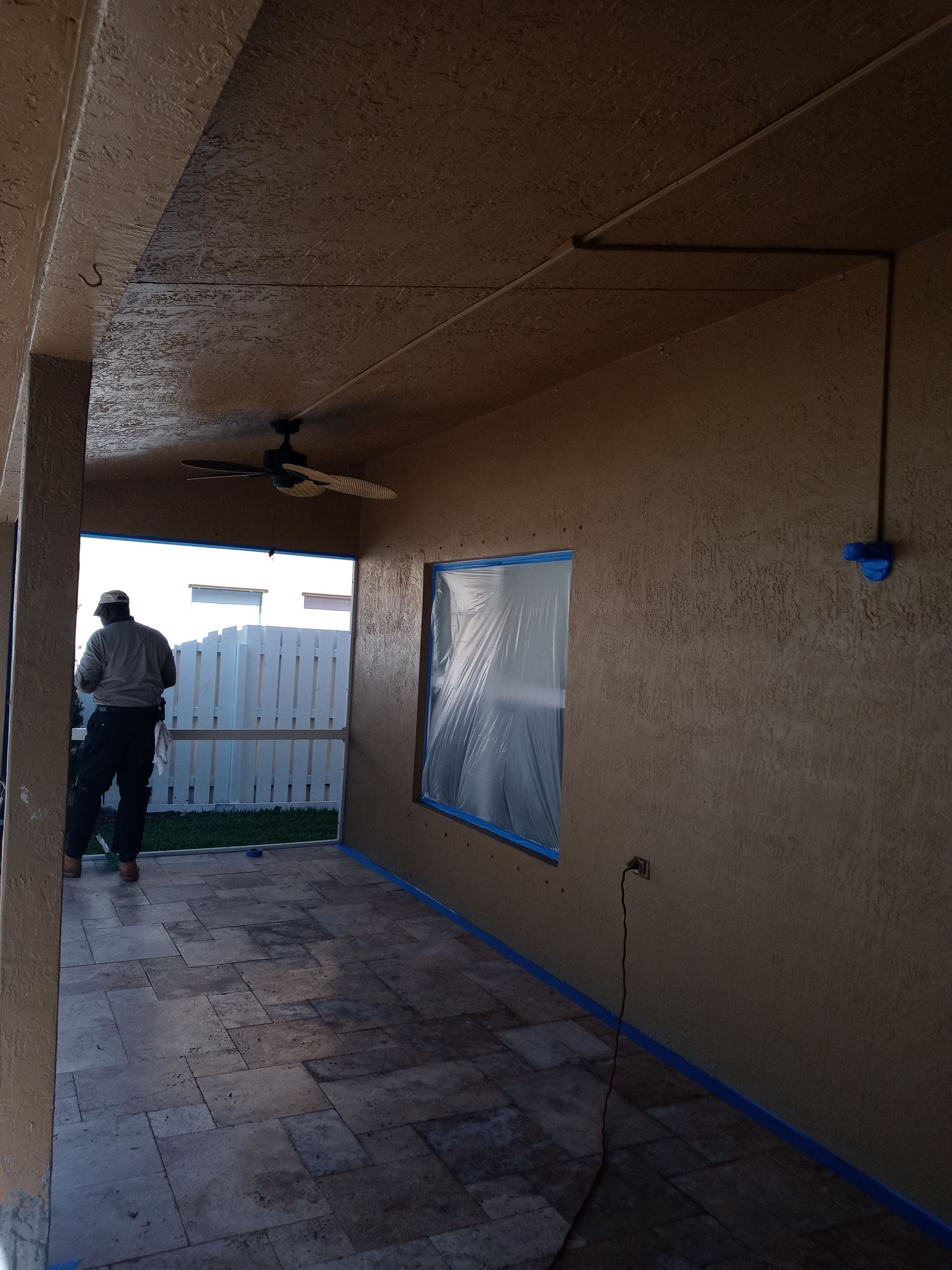 A man is standing on a porch painting a wall.