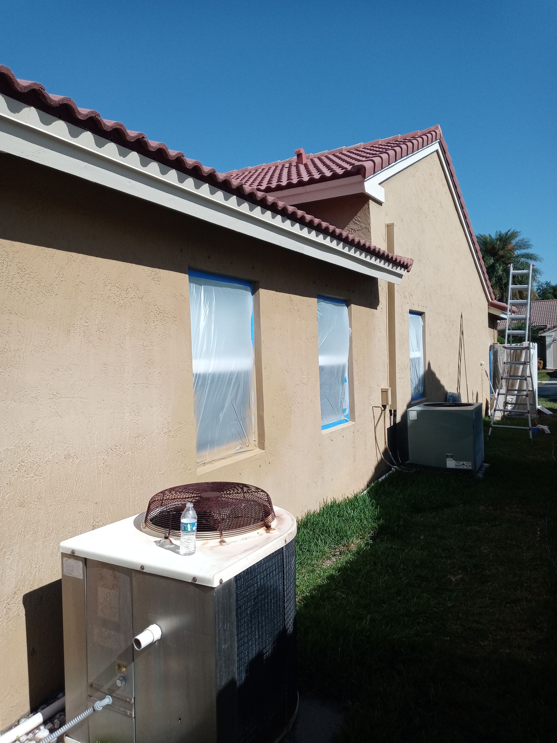 A house is being painted and there is a air conditioner on the side of the house.