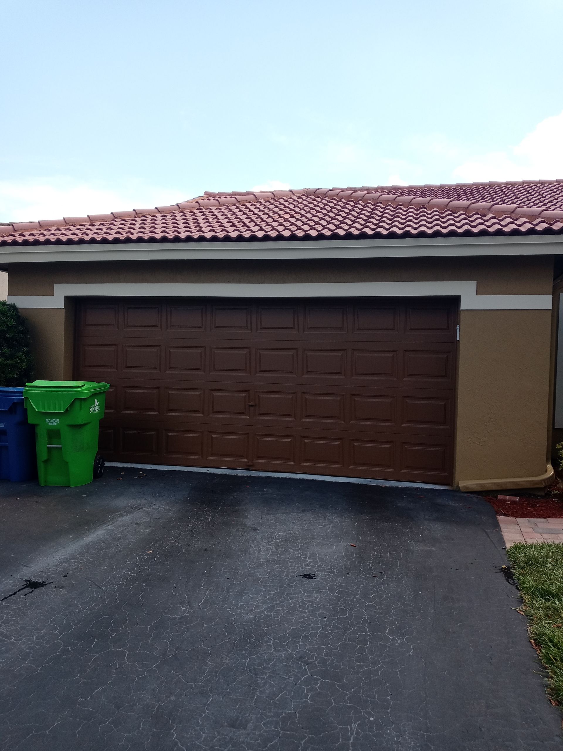 A brown garage door with two green trash cans in front of it