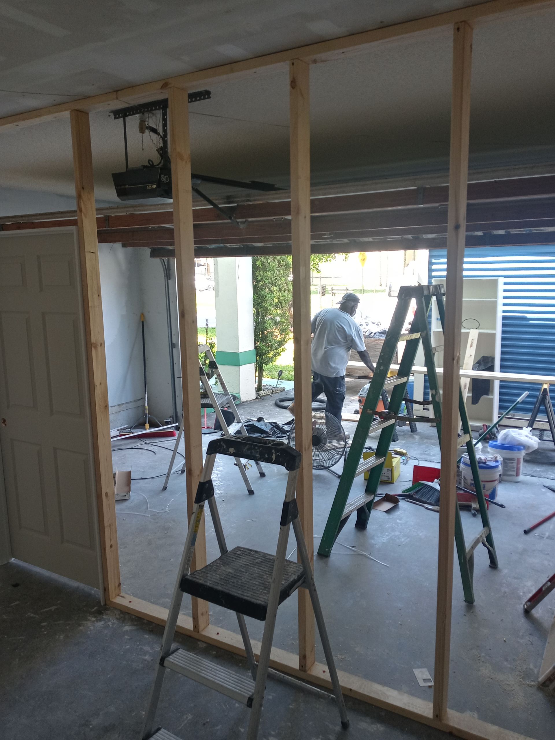 A man is working on a wall in a garage with a ladder.