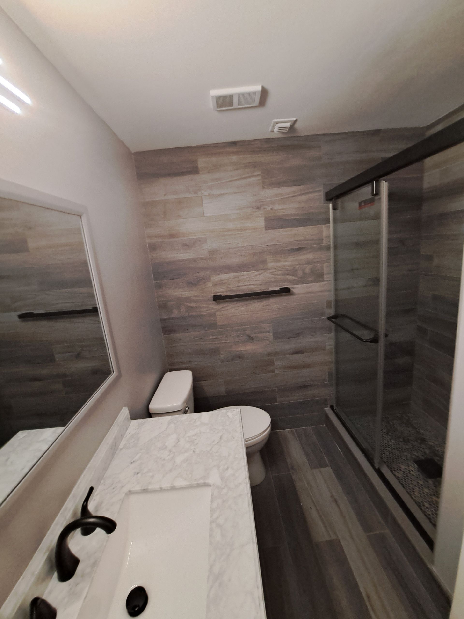 A bathroom with a toilet , sink , mirror and shower.