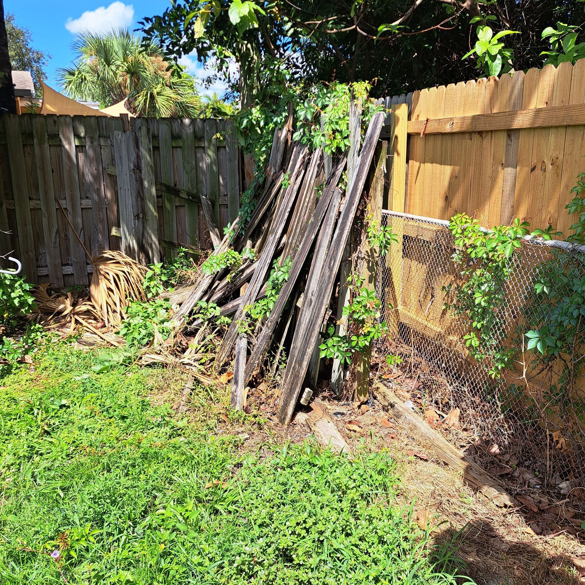 A pile of wood is sitting in the grass next to a wooden fence.