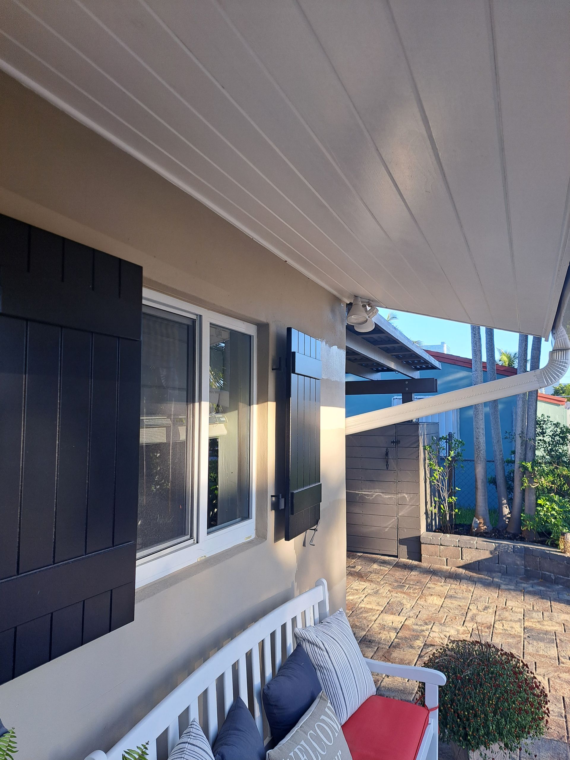 A porch with a bench and a window with black shutters