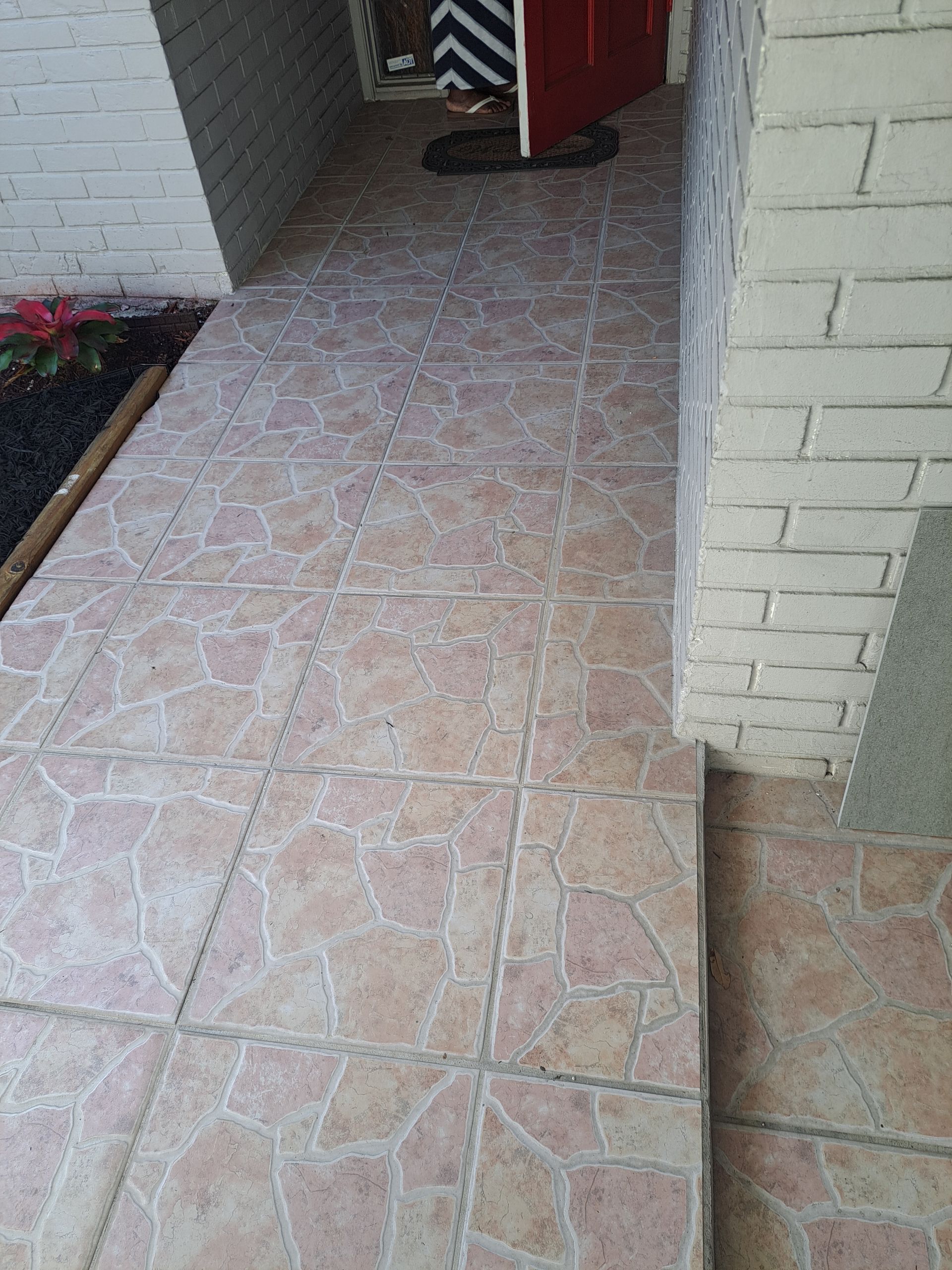 A tiled walkway next to a brick wall with a red door.