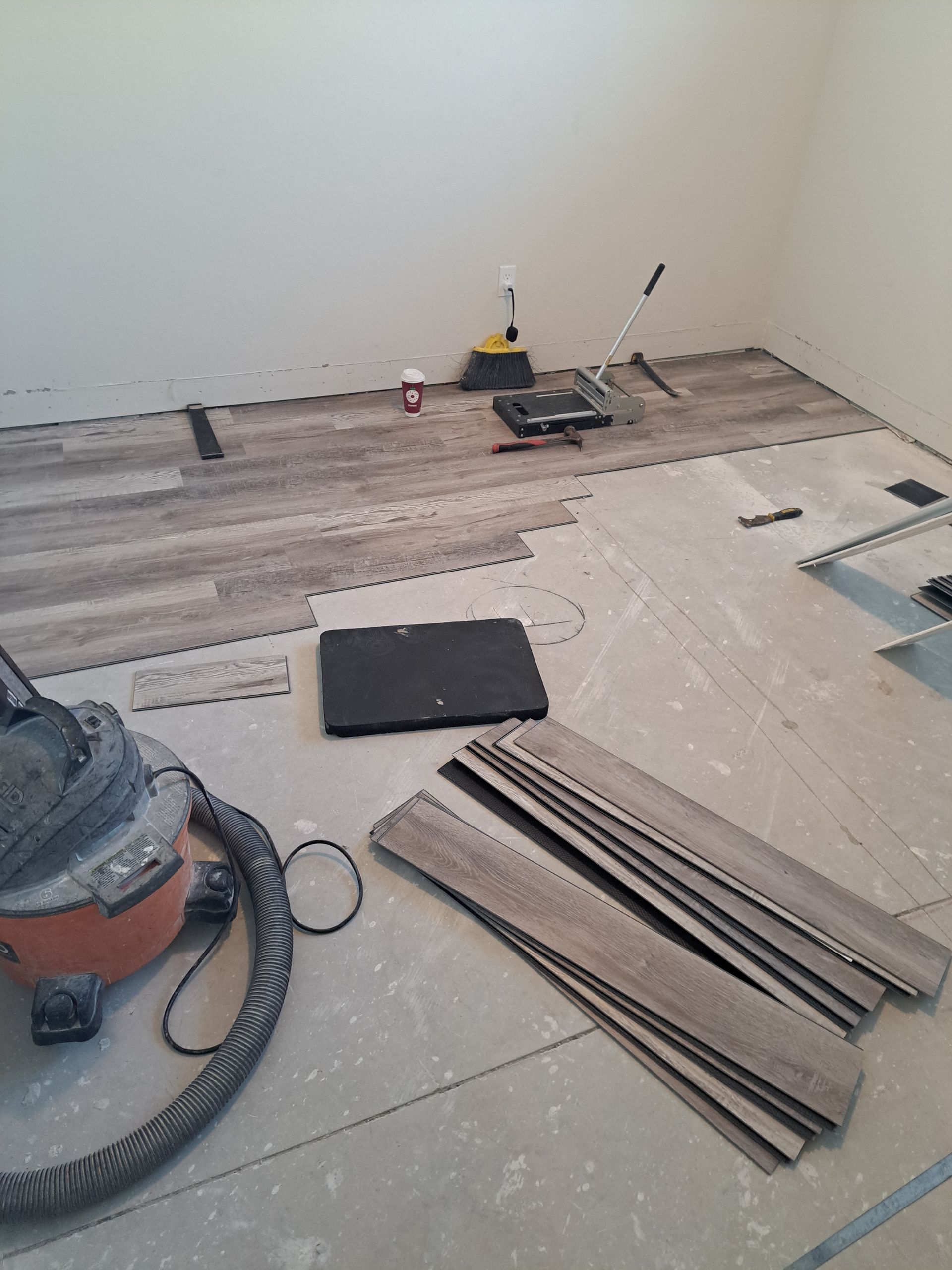 A room with a vacuum cleaner and a laptop on the floor.