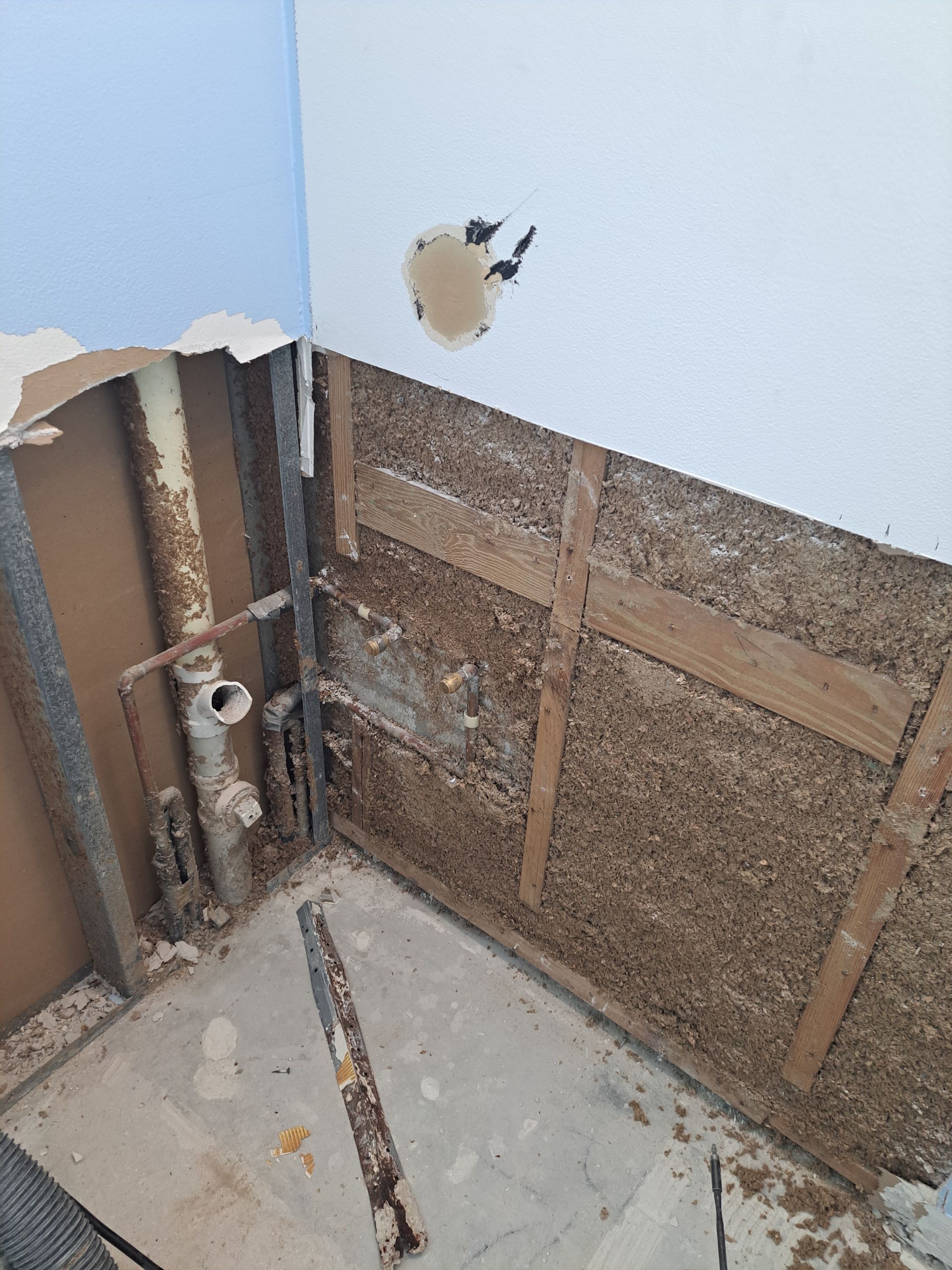A bathroom with a hole in the wall and pipes coming out of it.