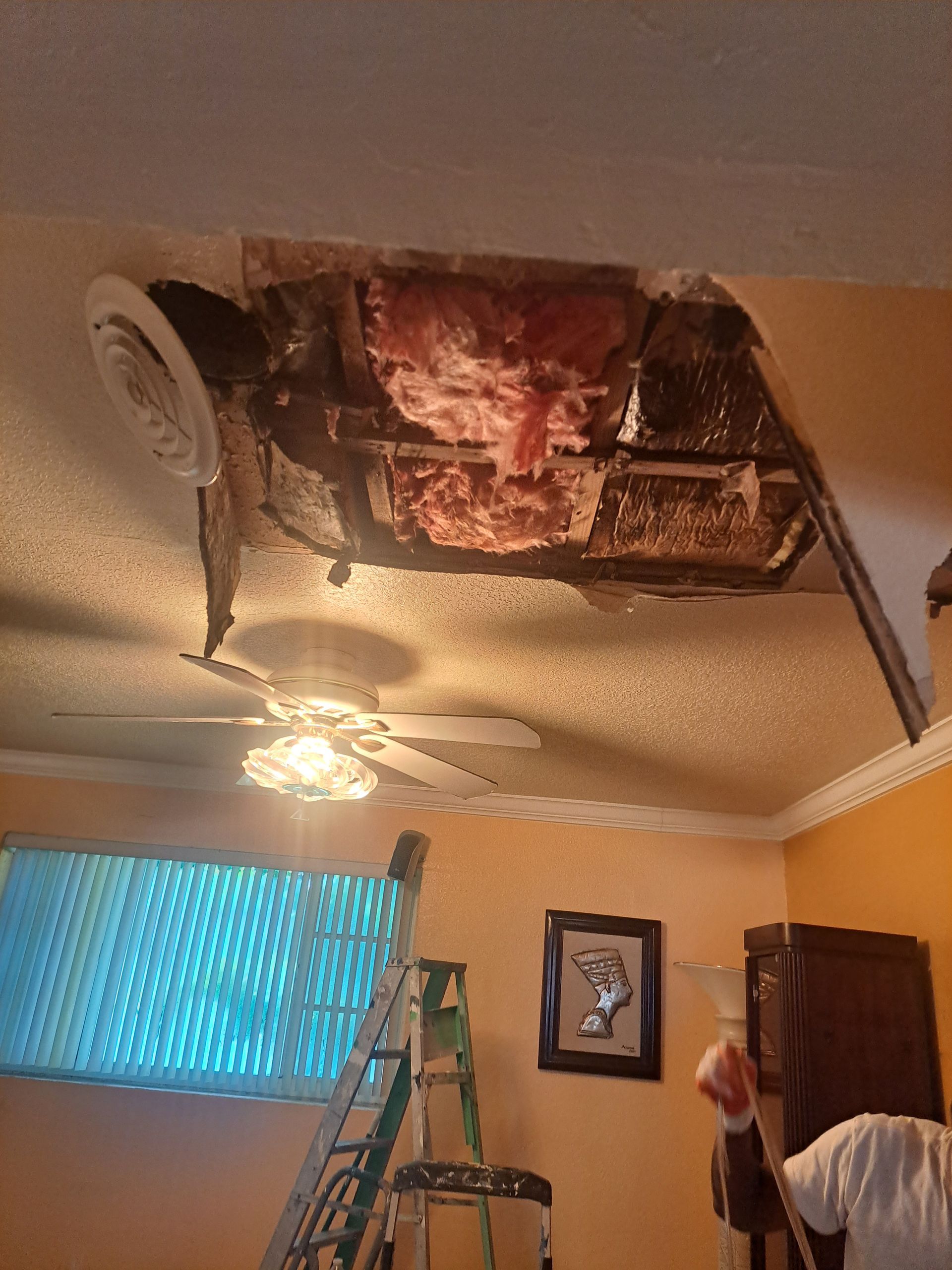 A room with a ceiling fan and a hole in the ceiling.