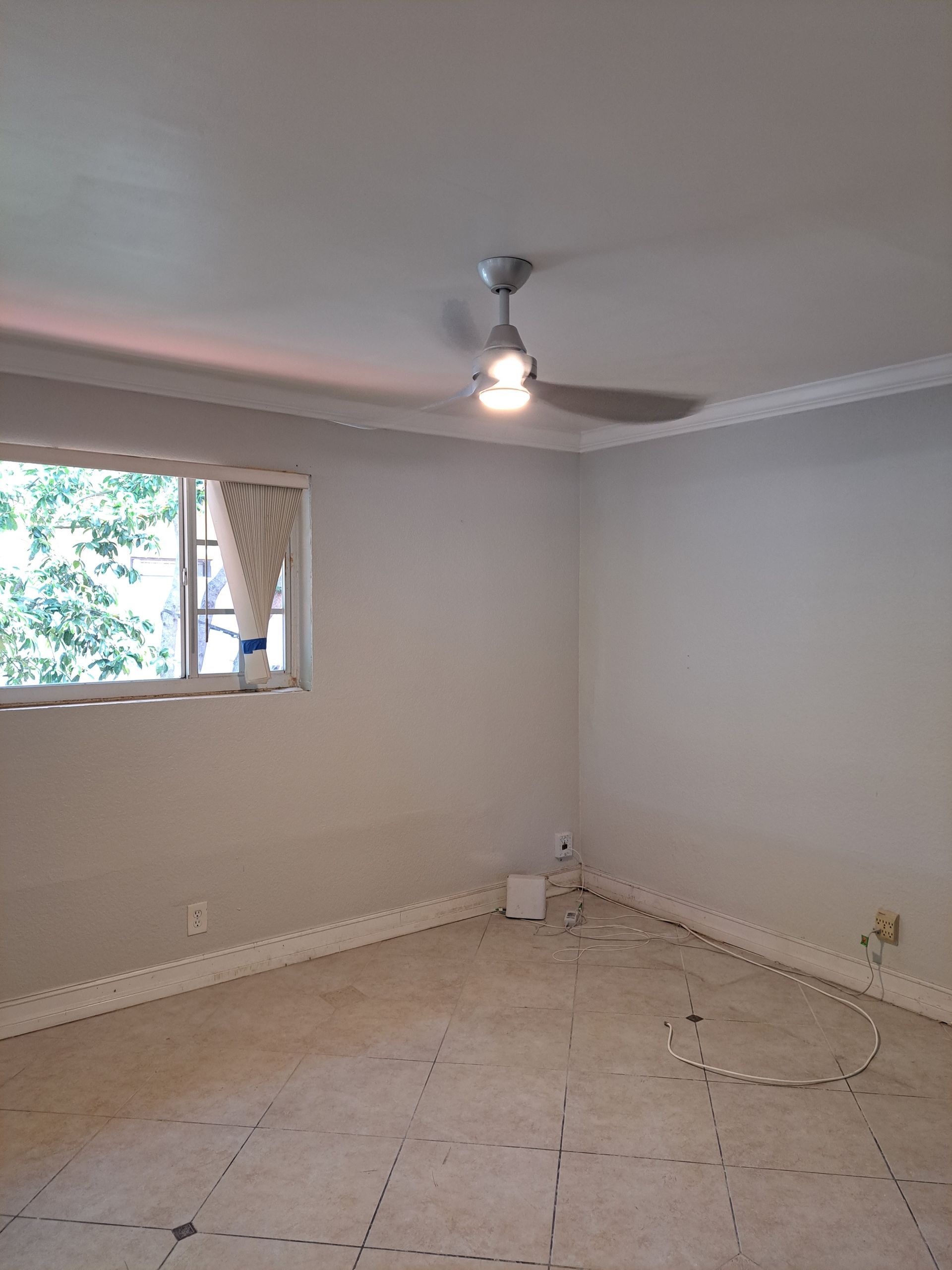 An empty room with a ceiling fan and a window.