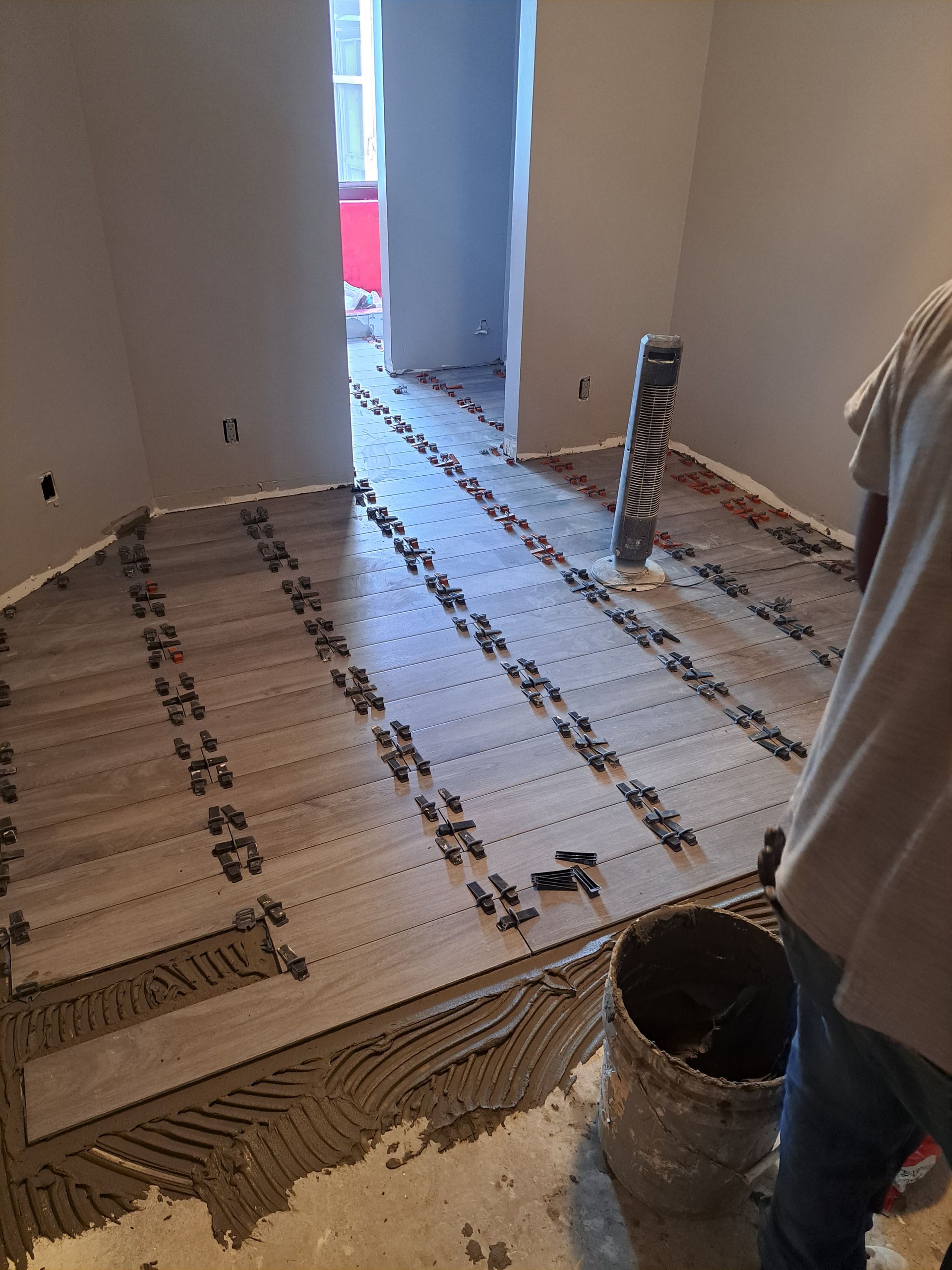 A man is standing in a room with a bucket of cement on the floor.