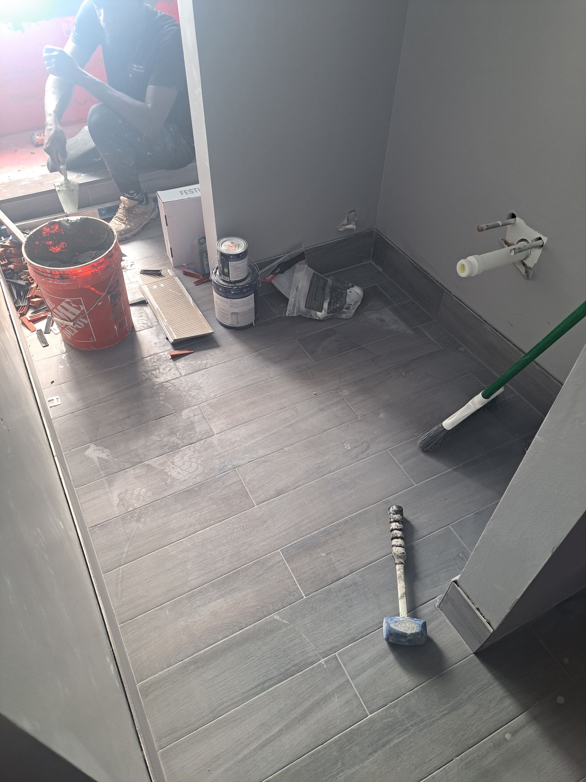 A man is sitting on the floor of a bathroom.