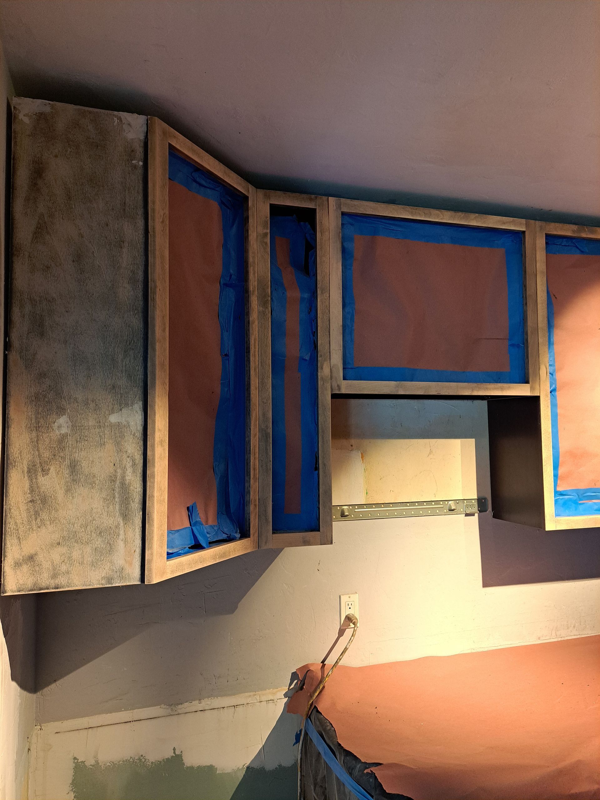 A person is painting a kitchen cabinet with blue tape