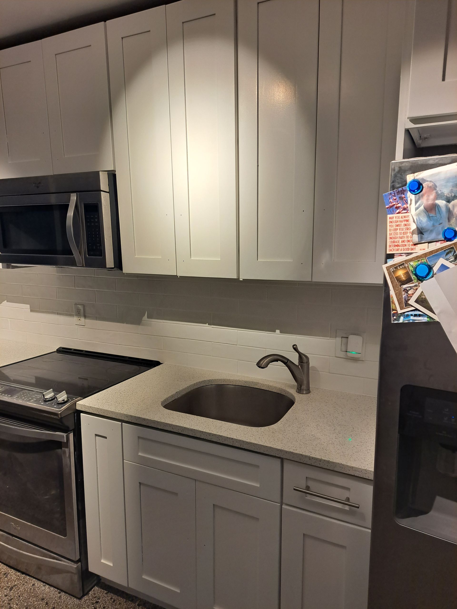 A kitchen with white cabinets , a sink , stove , microwave and refrigerator.