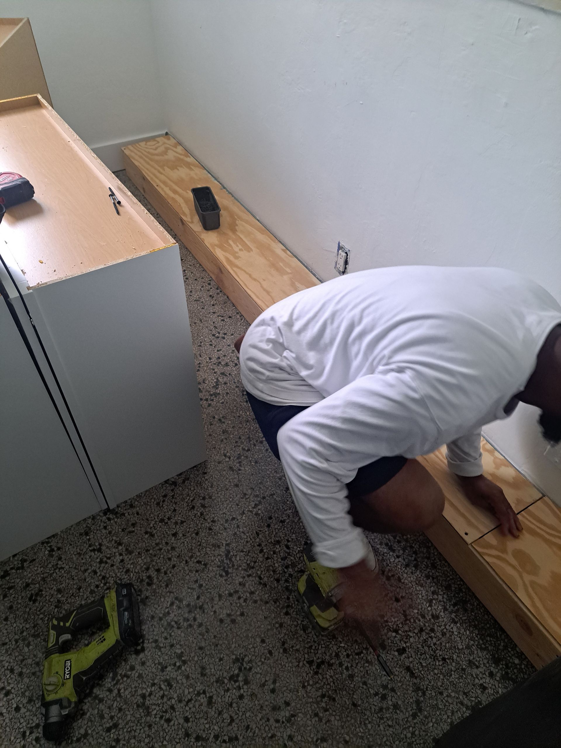 A man is kneeling on the floor working on a piece of wood.