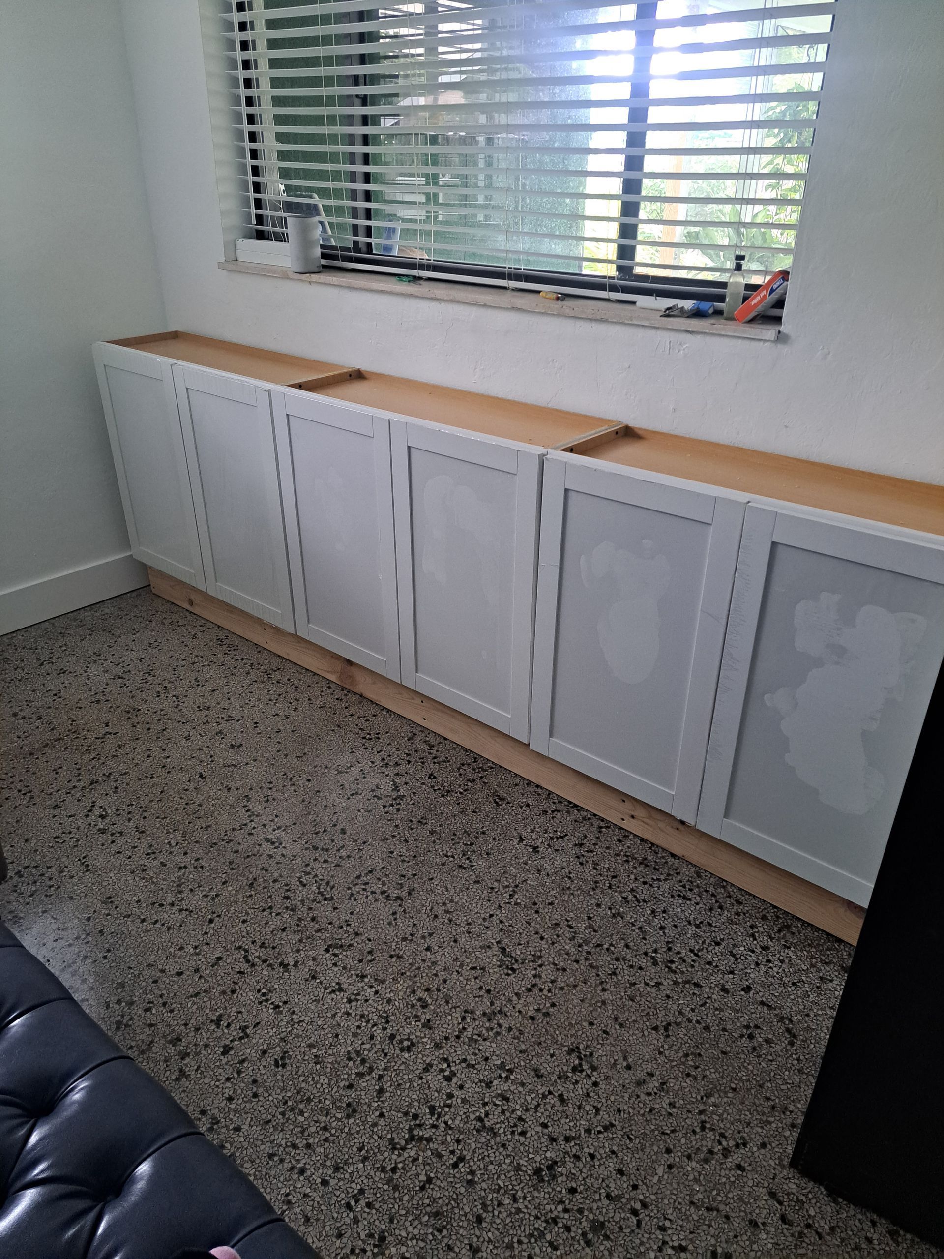 A room with white cabinets and a window with blinds.