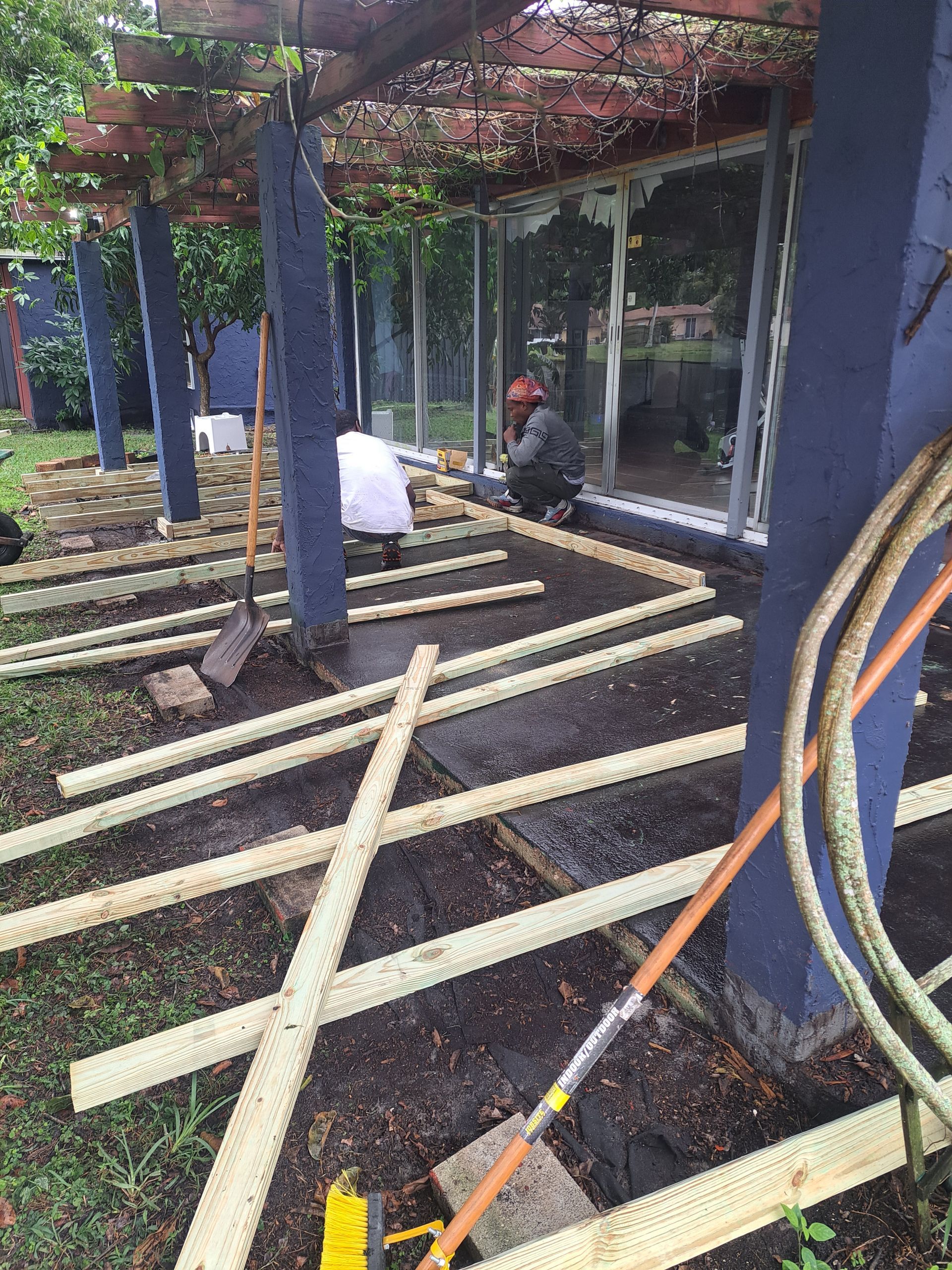 A man is working on a wooden deck under a pergola.