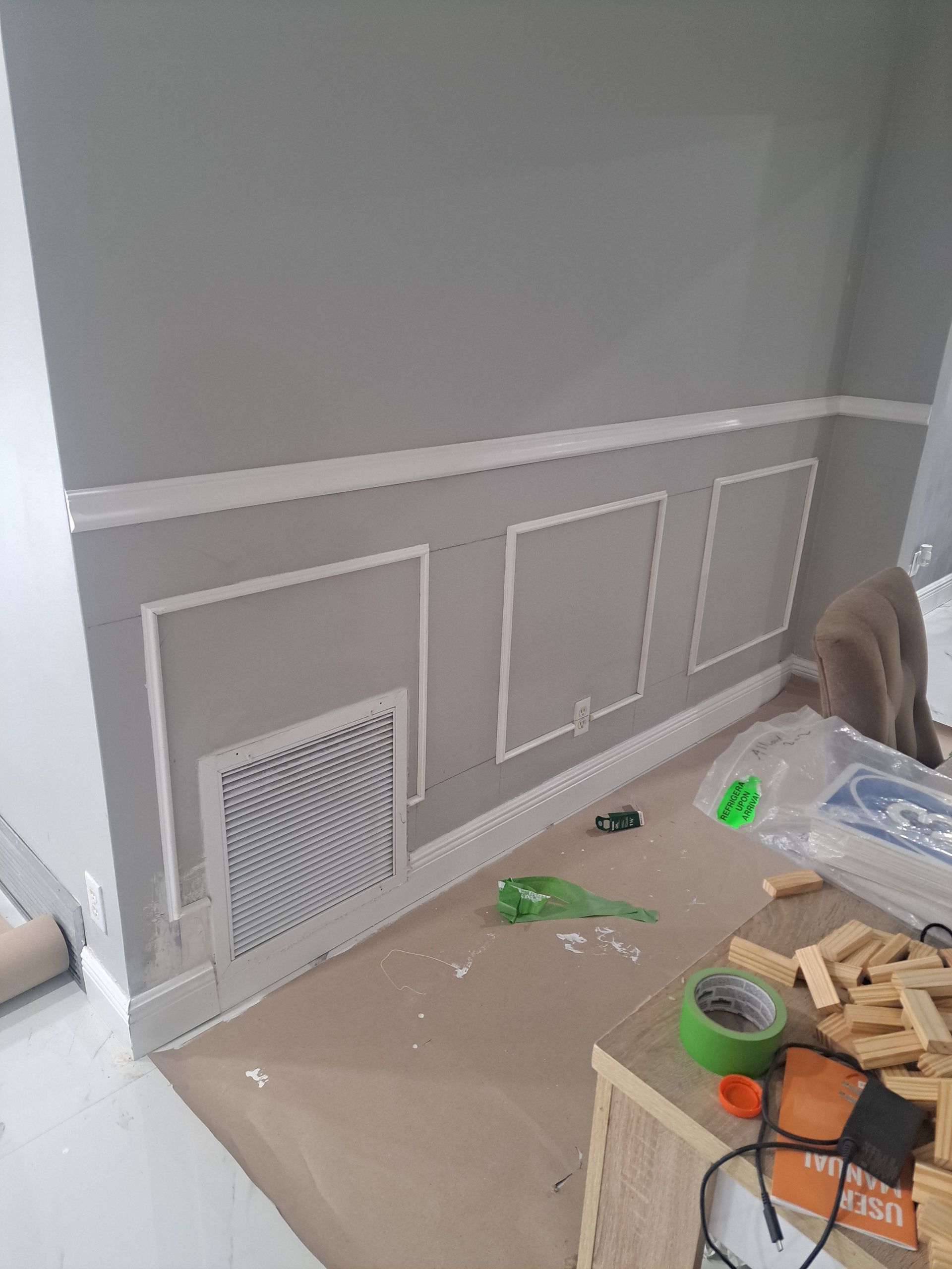 A room with a gray wall and a green tape measure on the floor.