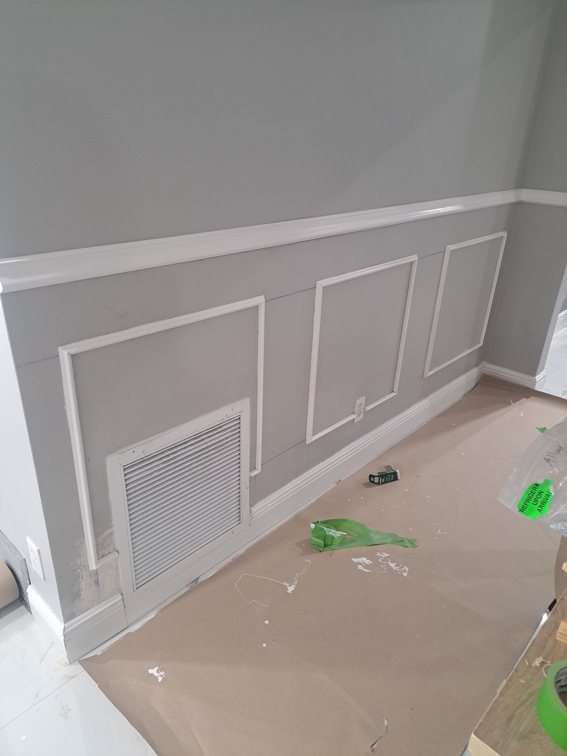 A room with gray walls and white trim is being painted.