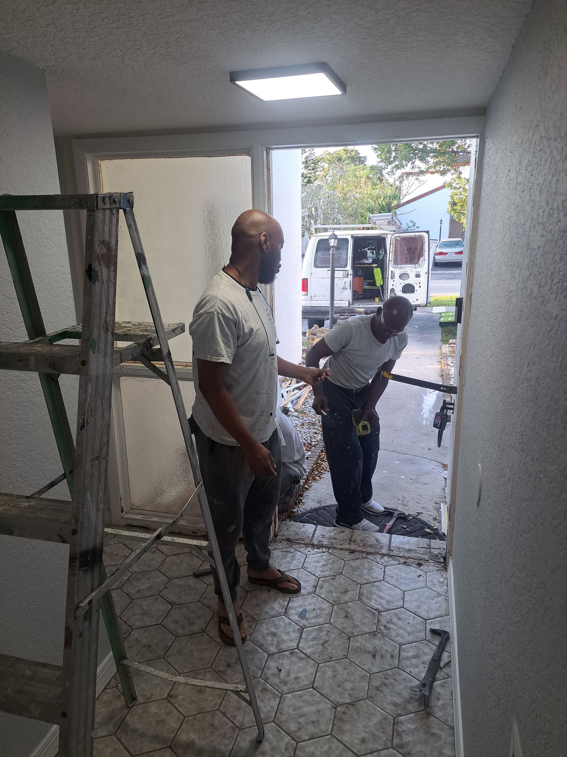 Two men are working in a room with a ladder.