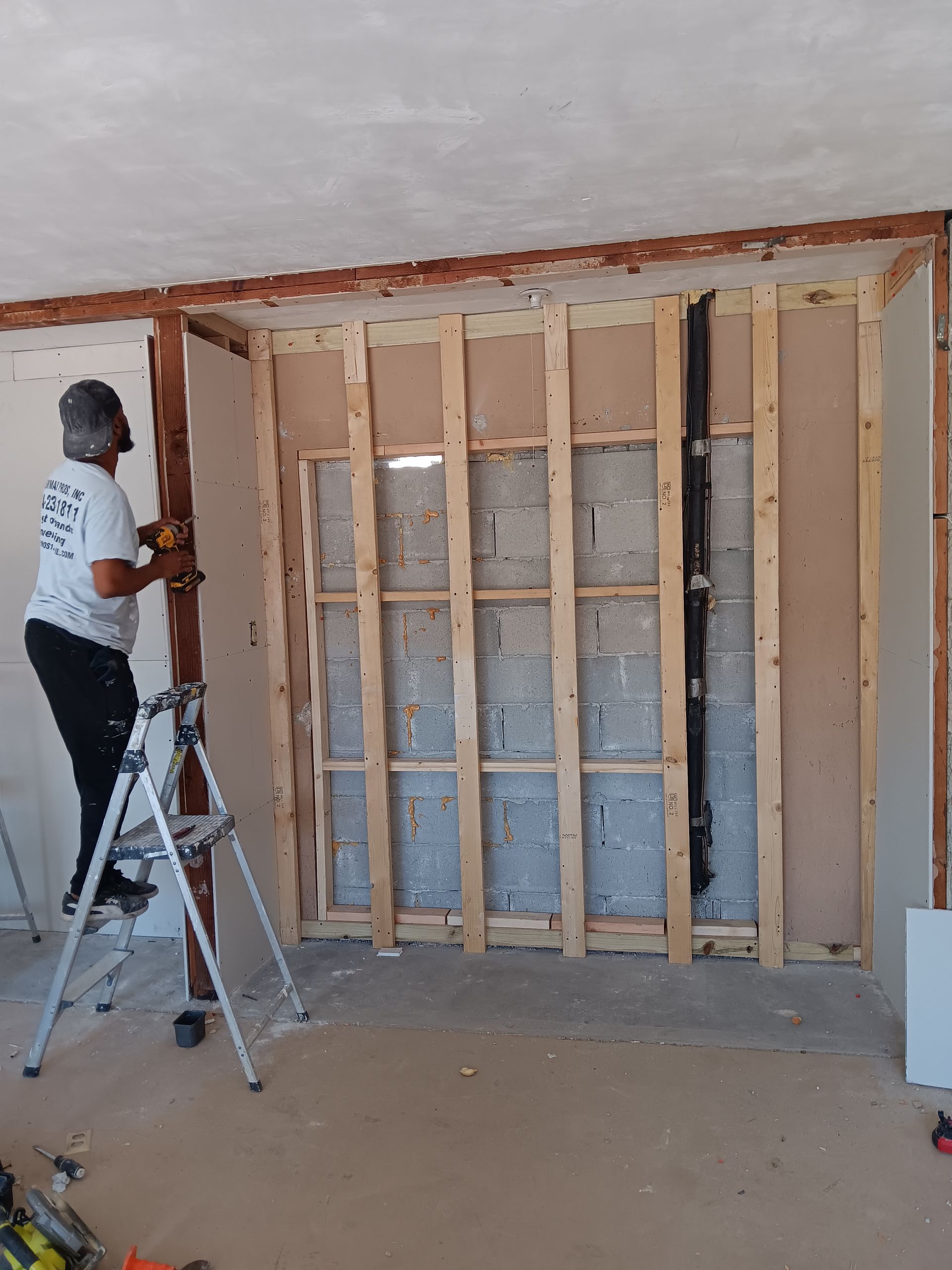 A man is standing on a ladder working on a wall.