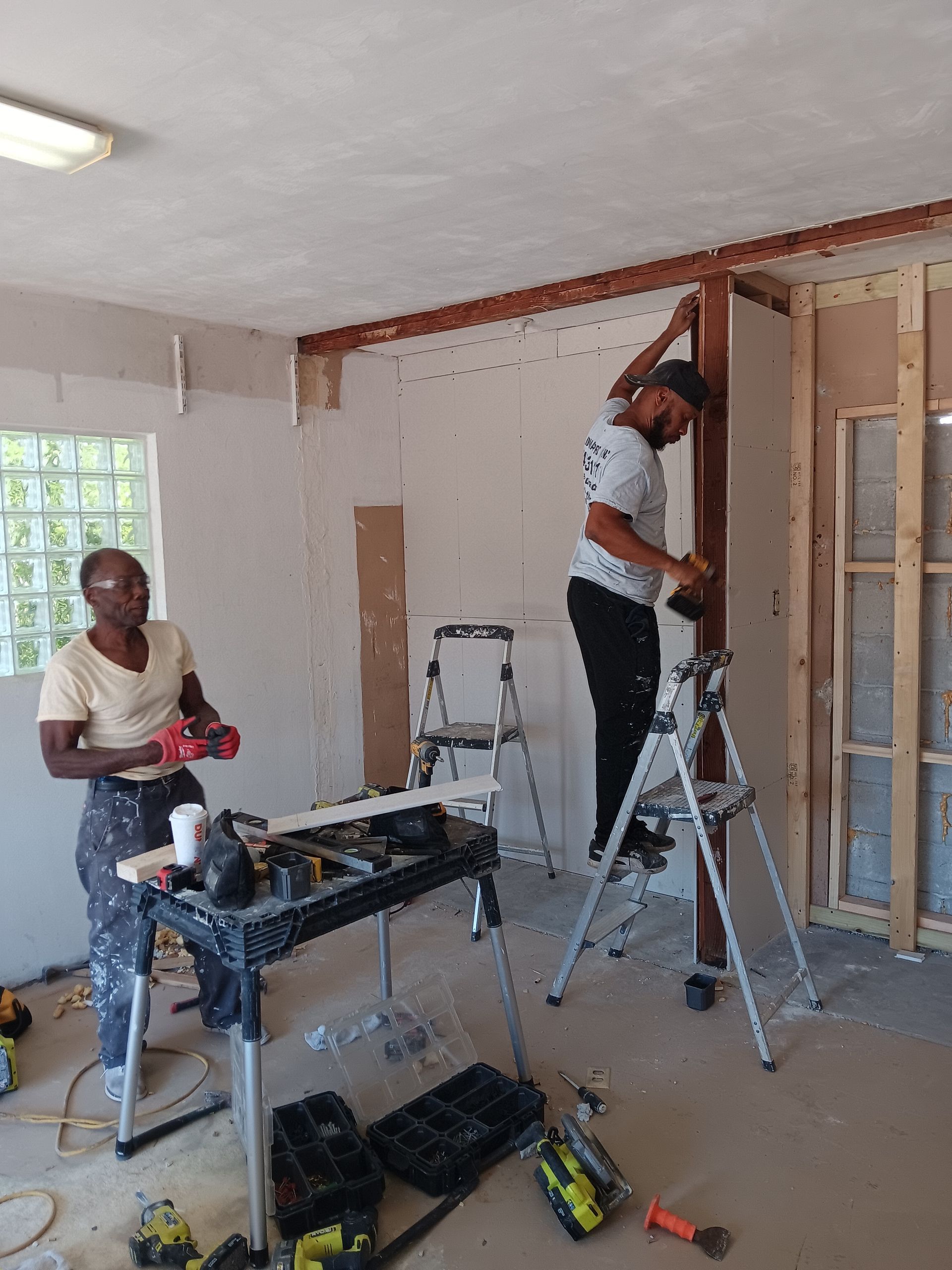 Two men are working on a wall in a room.