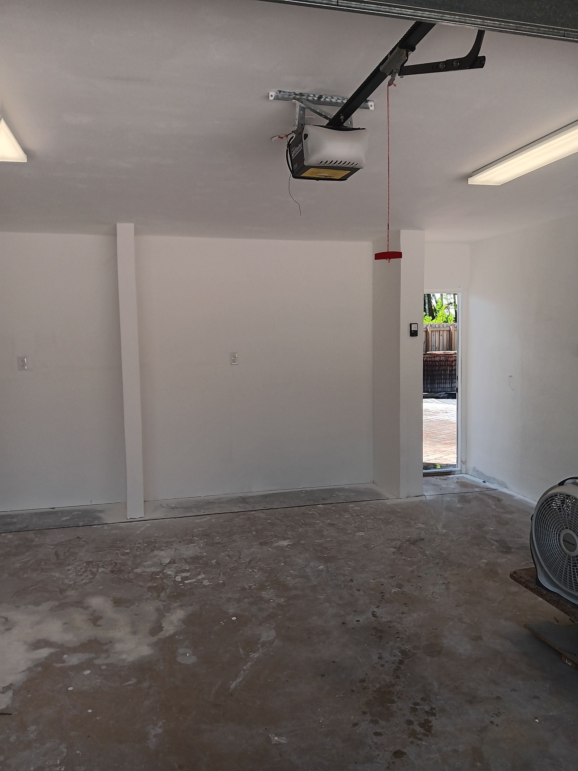 An empty garage with a garage door opener hanging from the ceiling.