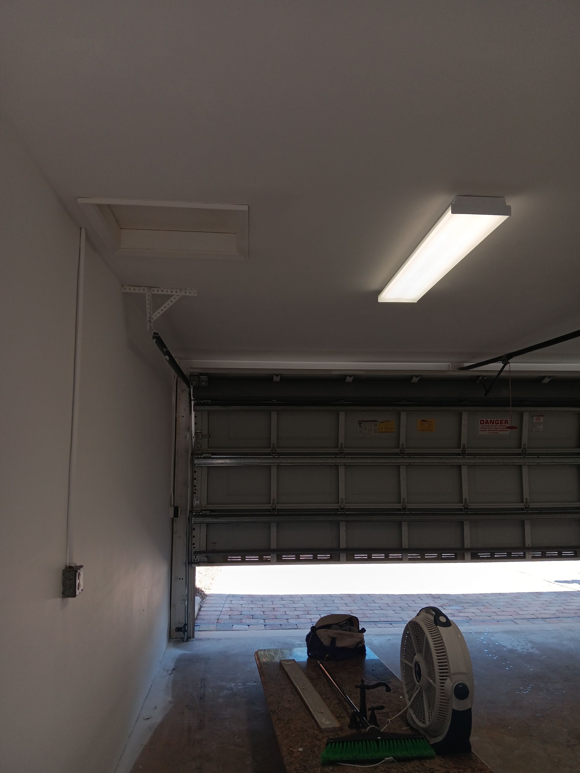 A garage with a garage door open and a fan on the floor.