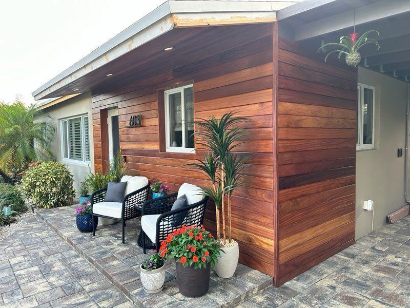 A house with a wooden siding and a patio with chairs and flowers.