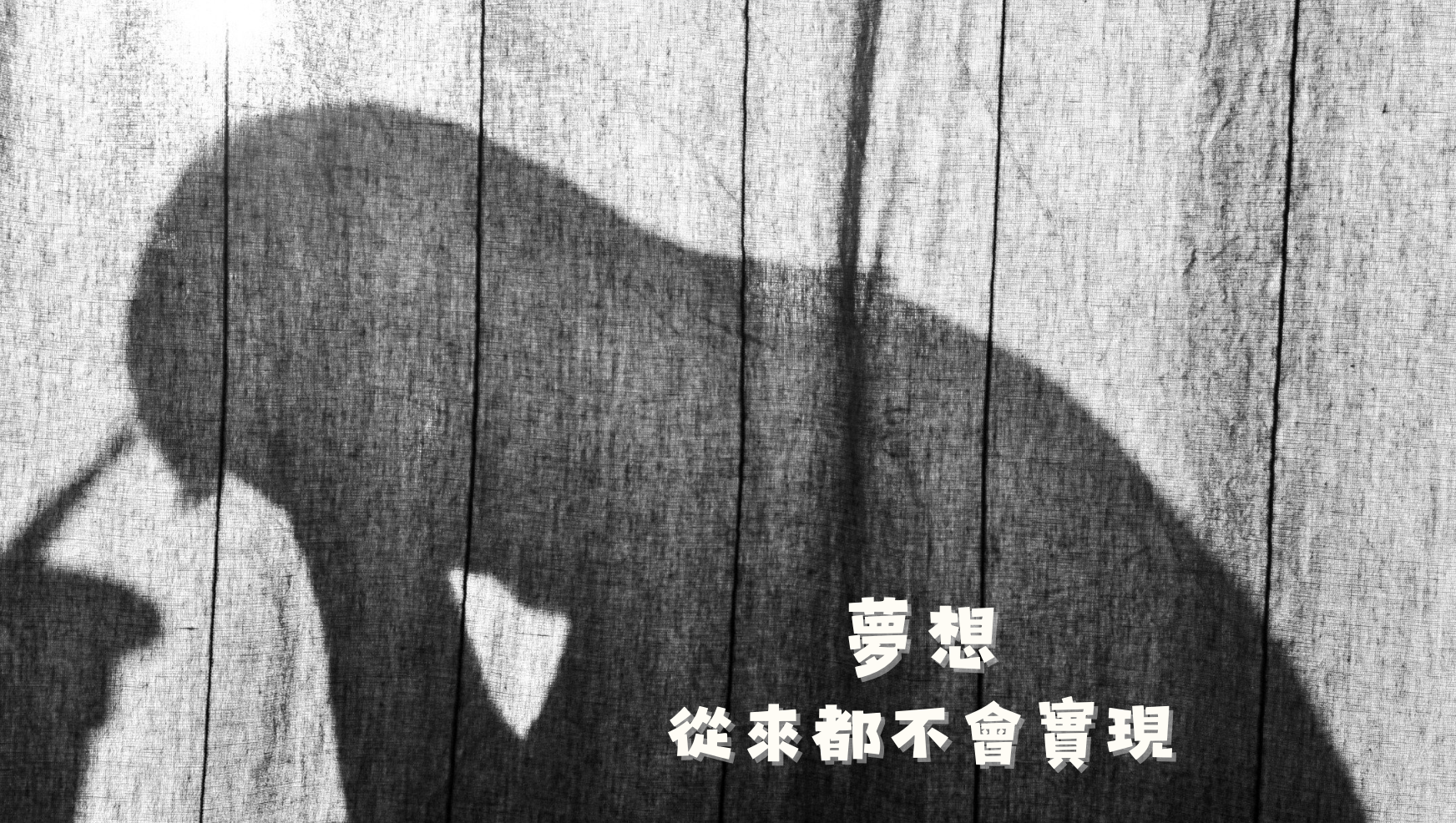 黑白照片中,一個人的影子低頭蜷坐在舊木板牆前,畫面疊加白色文字「夢想從來都不會實現」,象徵健康顧問風扇在找到上班族副業之前、月薪三萬覺得人生黑白的真實心境,為整篇故事拉開強烈的情緒對比。
