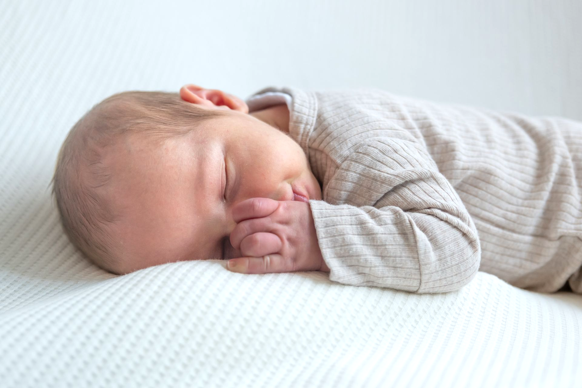 Een slapende baby ligt op een witte deken en rust met duimpje in mond
