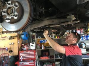 A Man is Working Under a Car in a Garage — Mechanical Servicesin Maroochydore, QLD
