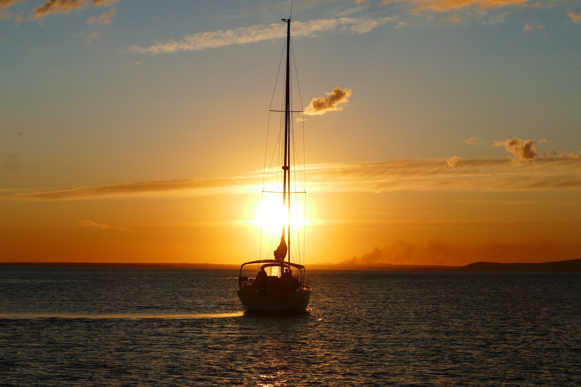 A sailboat is floating on top of a body of water at sunset.