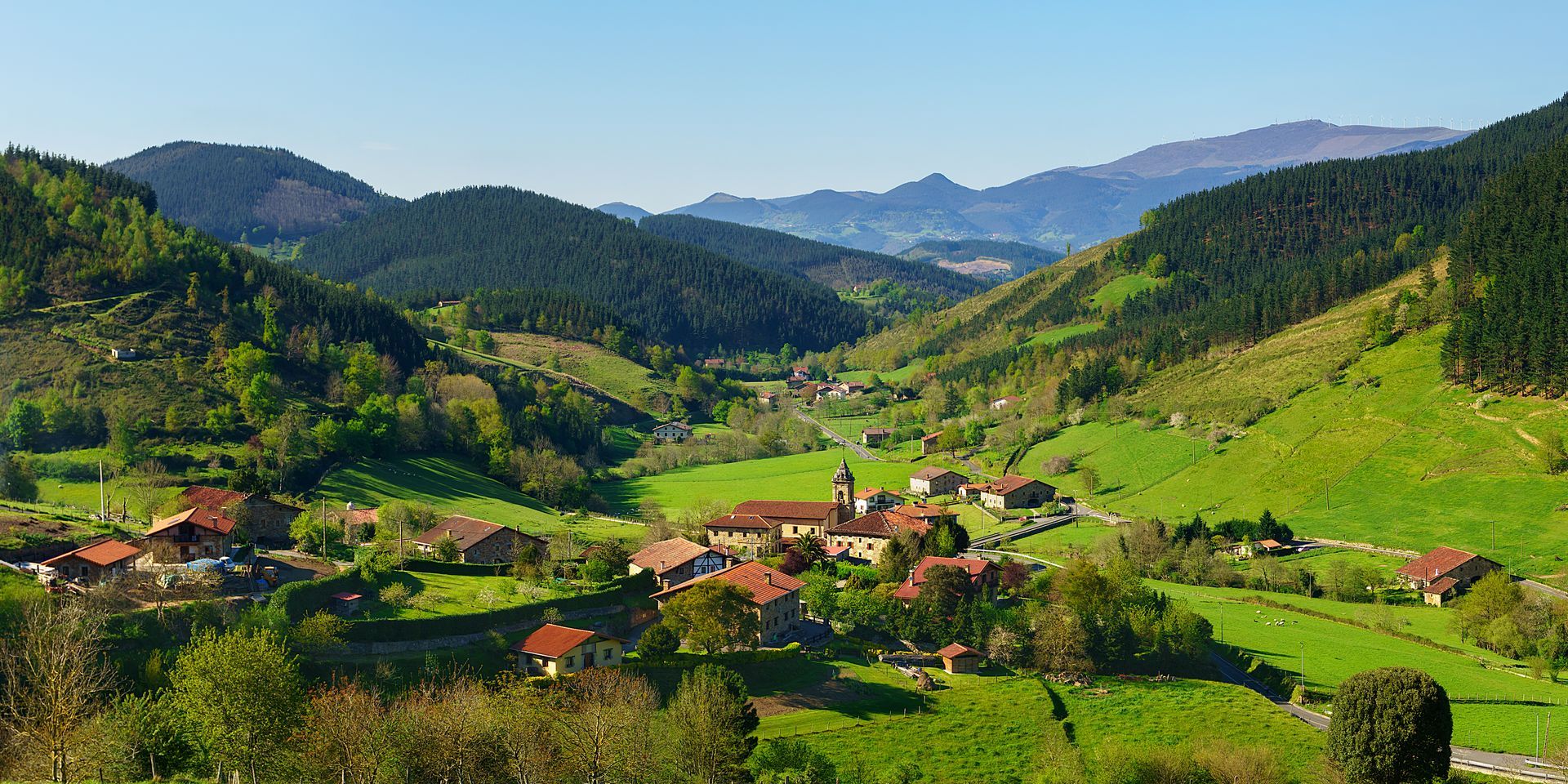 A small village in the middle of a lush green valley surrounded by mountains.