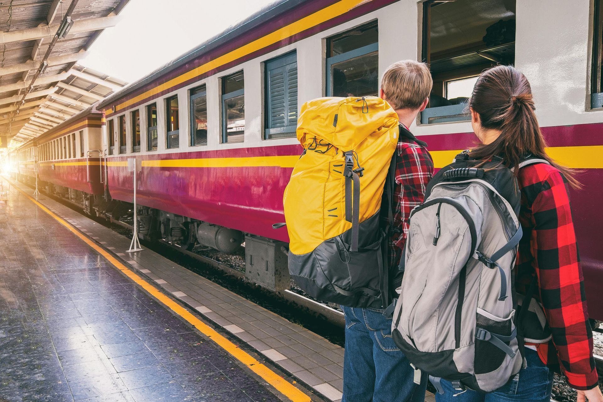 A man and a woman with backpacks are standing next to a train at a train station.