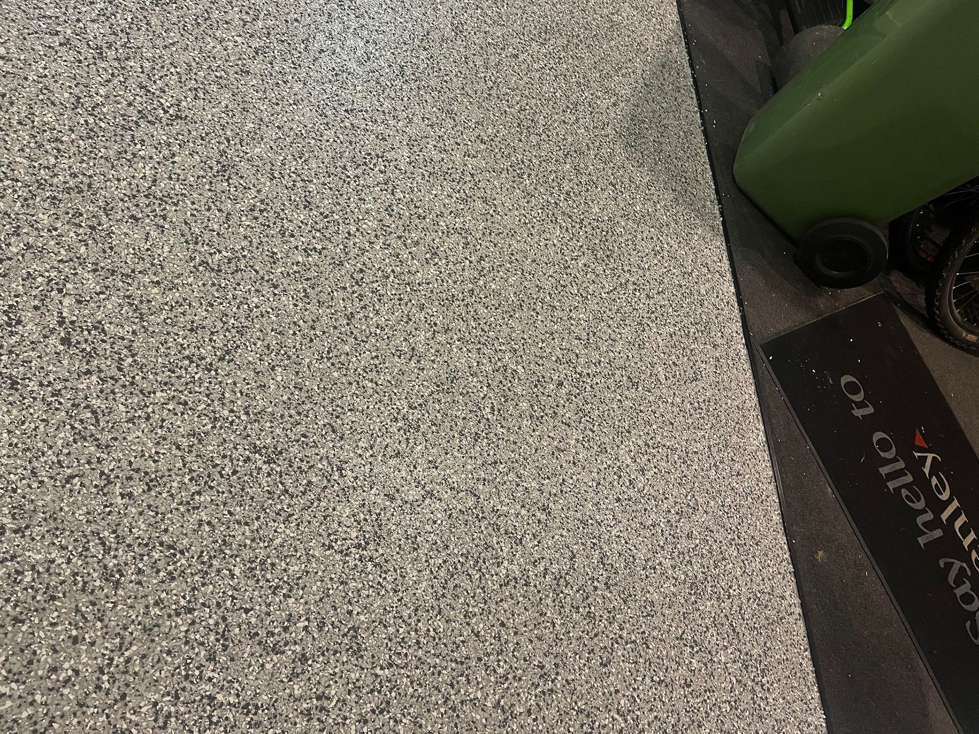 A close up of a gray floor with a green trash can in the background