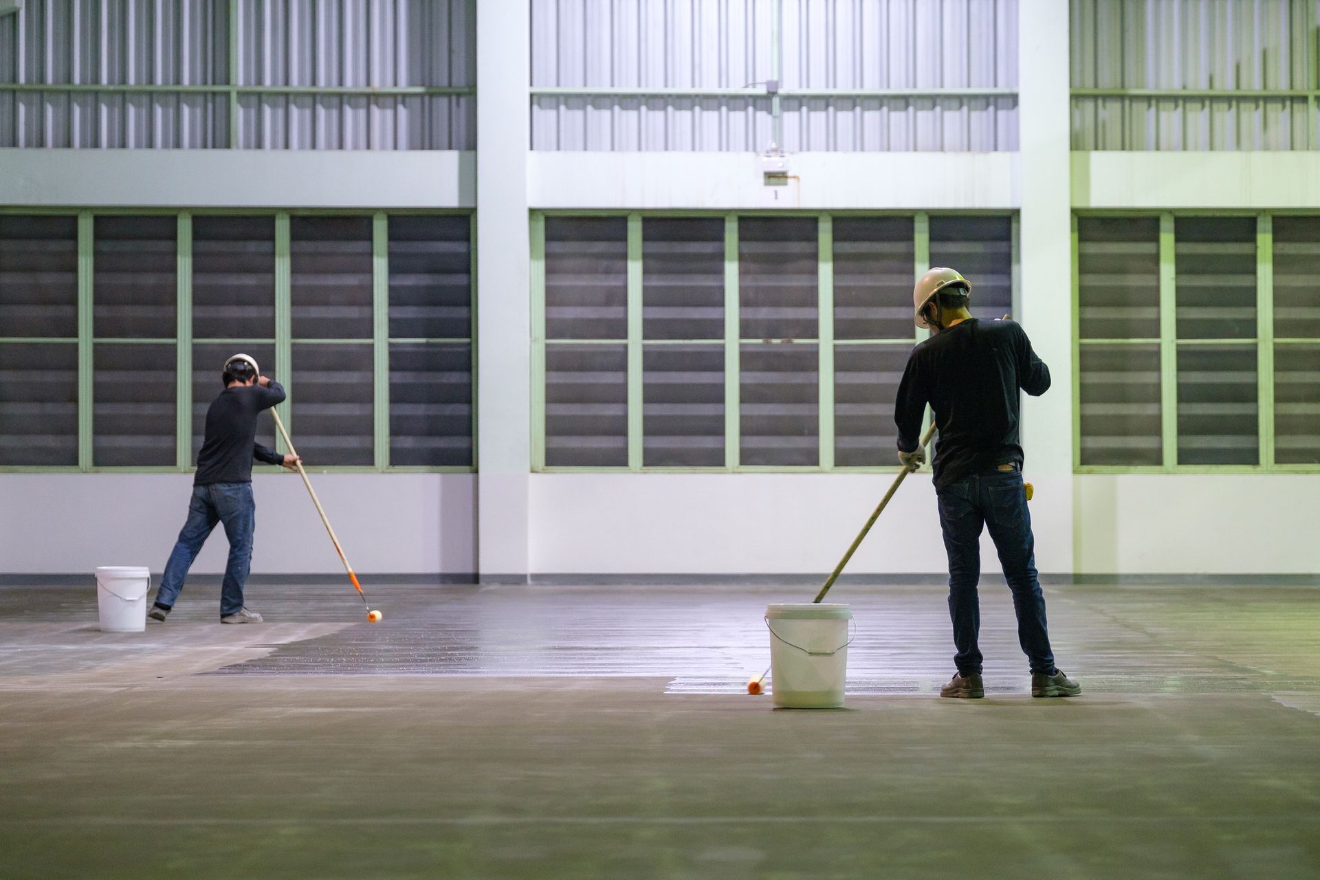Two men are painting a concrete floor in a warehouse