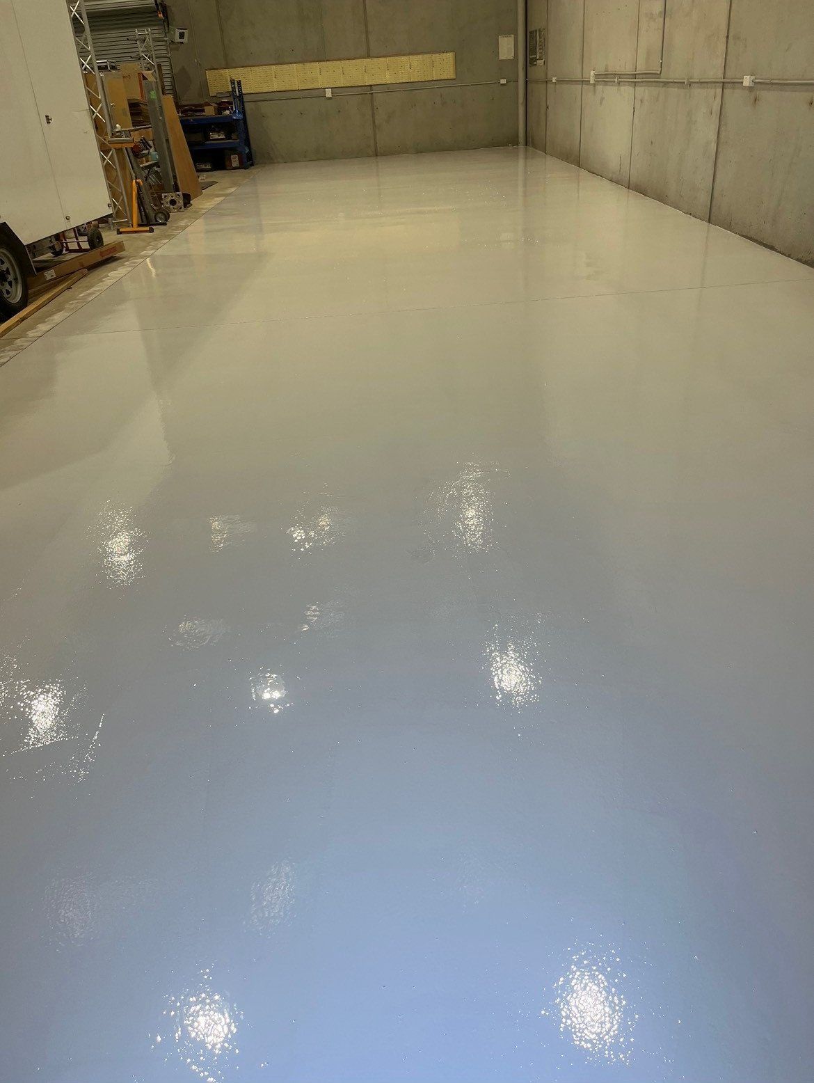 A warehouse with a white floor and a truck parked in the background