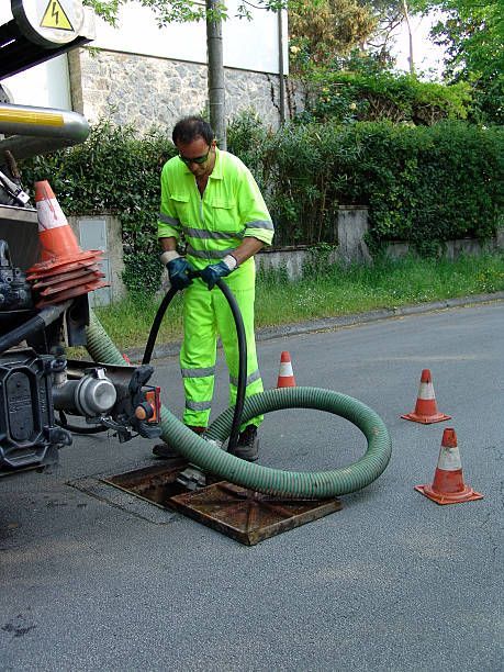 A man in a yellow jumpsuit is pumping water into a manhole cover.