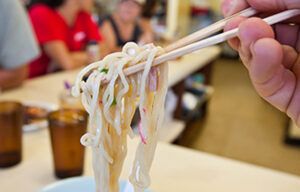 A person is eating noodles with chopsticks in a restaurant.