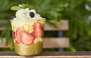 A glass filled with fruit and whipped cream is sitting on a wooden table.