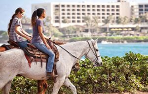 Two women are riding horses on a beach near the ocean.